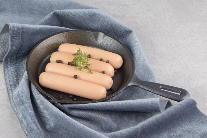 Four pinkish shrimp jello sausages in a pan garnished with herbs and peppercorns on a blue cloth background