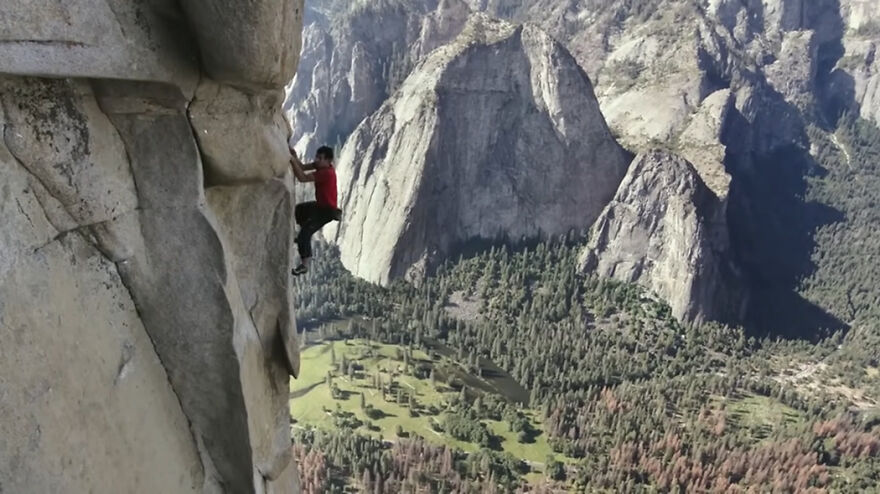 Man in red shirt rock climbing a steep cliff, illustrating scenes from movies based on true stories that seem unbelievable