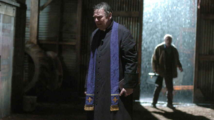 A tense scene from a movie based on true stories, featuring a man in religious robes in a dimly lit industrial setting.