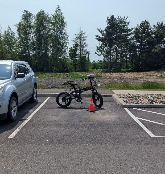 Bike parked in a car parking spot with a traffic cone, highlighting people allergic to acting like sensible adults.