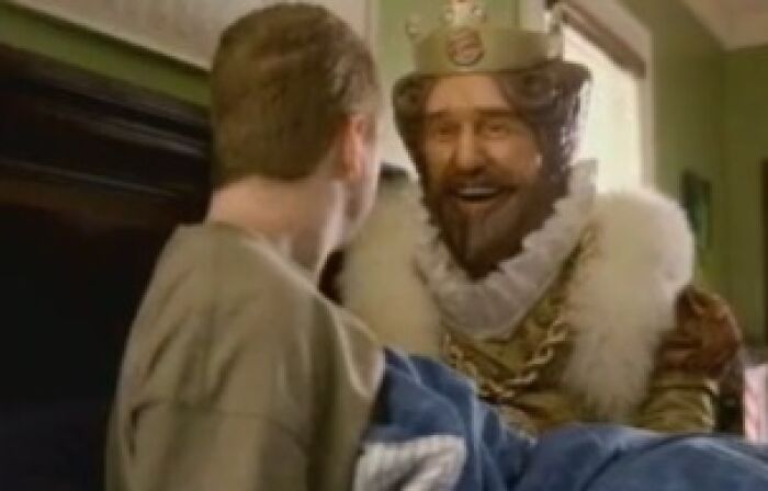 Man dressed as a king wearing a crown and fur collar talking to a boy in a dimly lit room, creepy commercials theme.