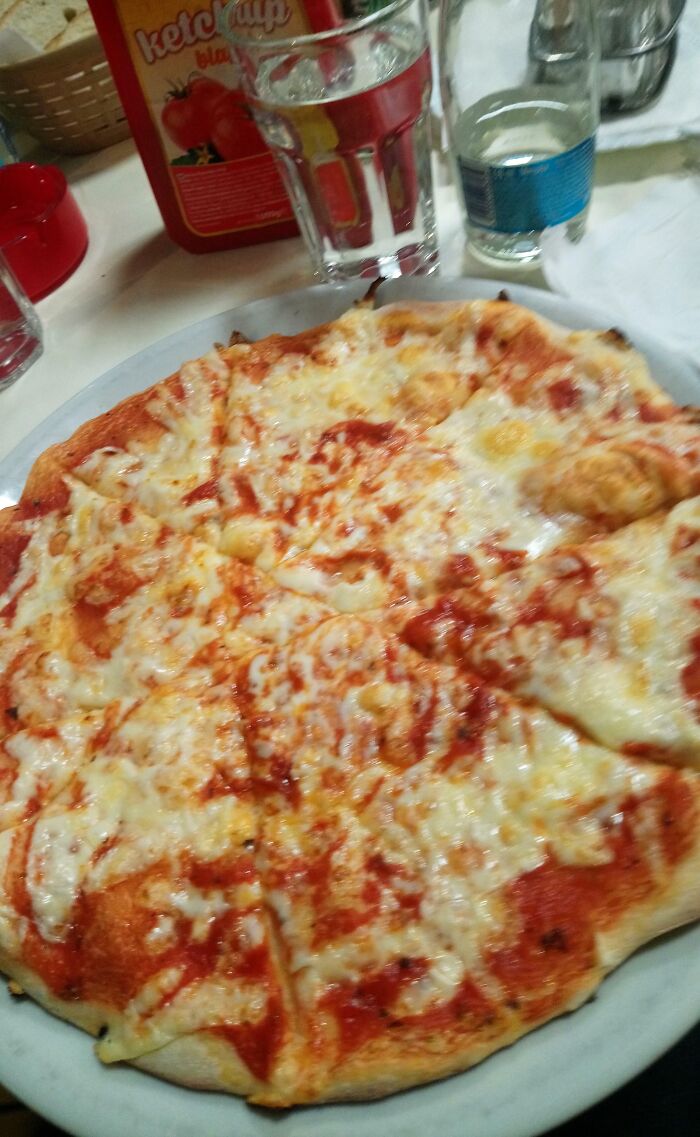 Cheese pizza on white plate with water glass and ketchup bottle, illustrating people allergic to acting like sensible adults.