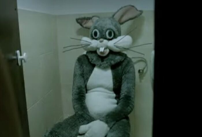 Person in a creepy rabbit costume sitting in a small bathroom stall, evoking eerie and unsettling commercial imagery.