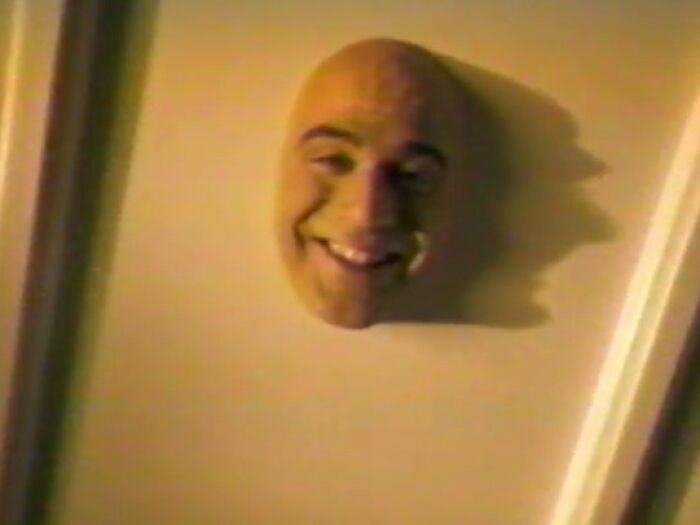 Creepy commercial featuring a floating smiling head mounted on a wall casting a shadow in dim lighting.