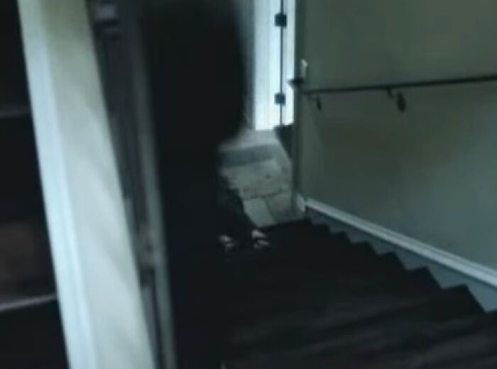 Shadowy figure descending dark stairs in a dimly lit hallway, evoking creepy commercial nightmare vibes.