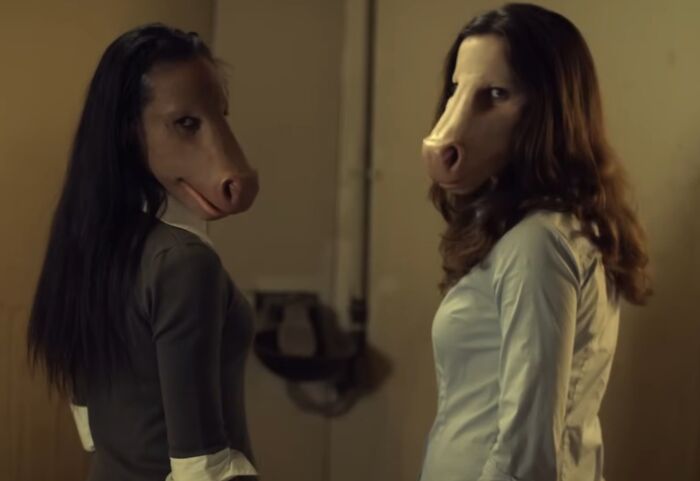 Two women wearing creepy horse masks in a dimly lit room in a scene from creepy commercials.