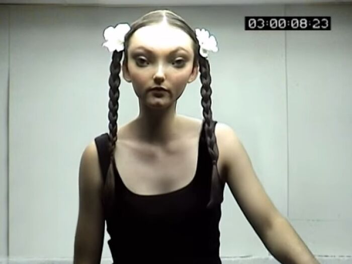Woman with braided hair and flowers wearing a black top in a dimly lit setting from creepy commercials.