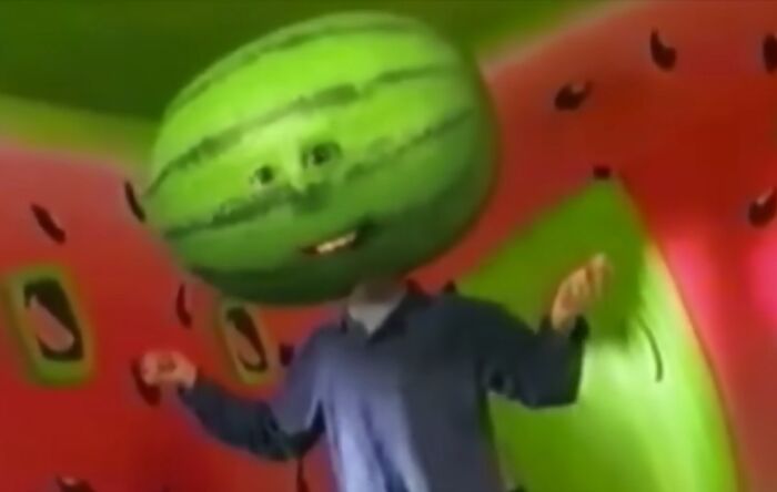 Person wearing a watermelon head in a colorful room, one of the creepy commercials that might give you nightmares.