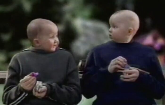 Two unnerving children with rigid necks sitting on a bench, evoking creepy commercials that might give you nightmares.