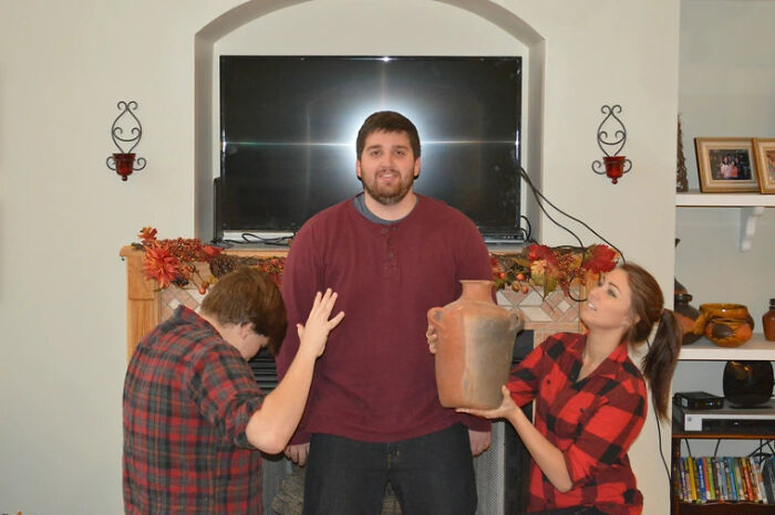 Family photo with two children awkwardly posing around father holding a large vase, creating a funny and cringed moment online.