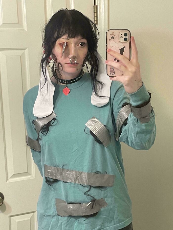 Person wearing a genius Halloween costume with duct tape, fake wounds, and attached hair, taking a selfie in a mirror.