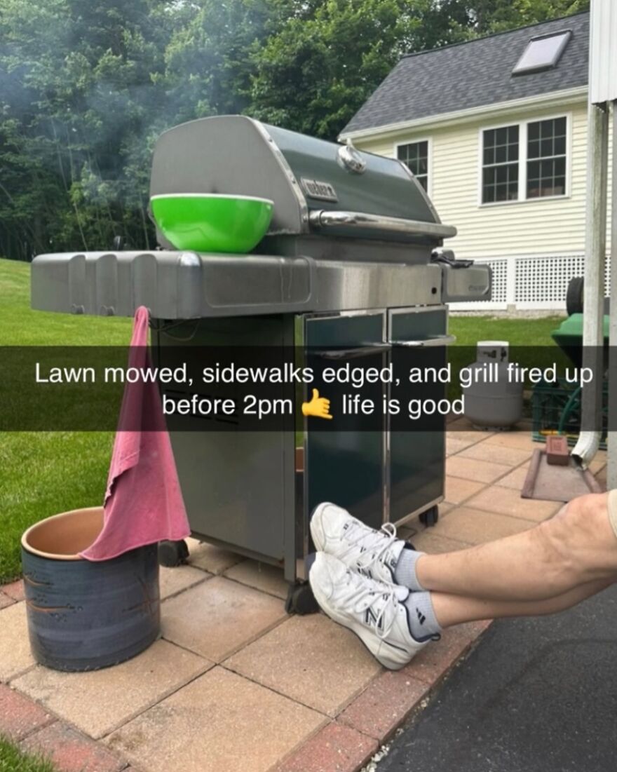 Outdoor grill fired up with legs resting nearby, showcasing typical dad humor and chores in a backyard scene.