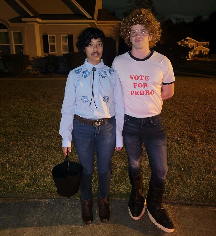 Two people wearing genius Halloween costumes outside at night, one holding a bucket and the other in a Vote for Pedro shirt.