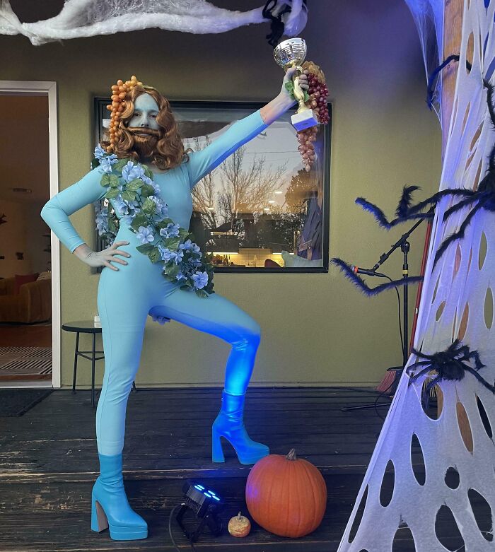 Person in a creative Halloween costume with blue bodysuit, flowers, grapes, and pumpkin, showcasing genius Halloween costumes.