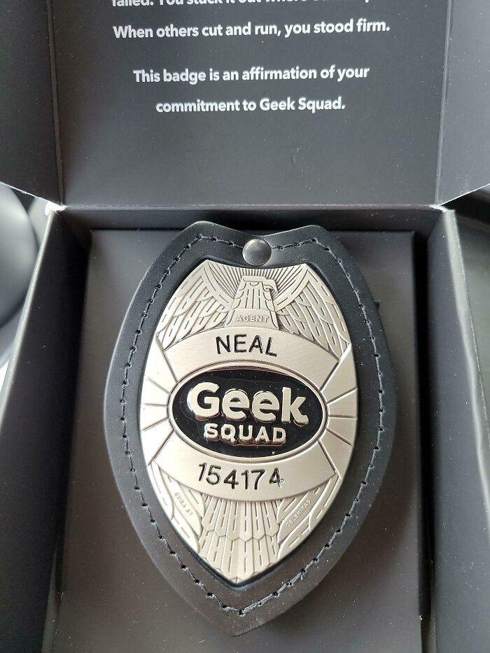 Geek Squad agent badge with the name Neal and badge number 154174 displayed in a black leather holder.
