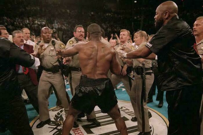 Boxer in black shorts surrounded by security during a heated moment captured in fascinating photos and stories.