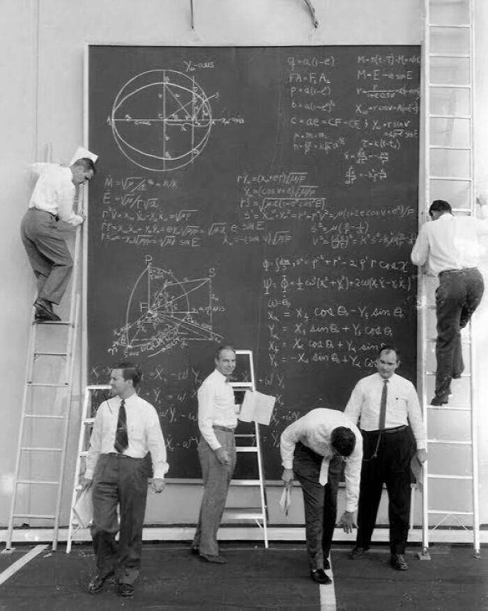 Men solving complex equations on a large blackboard with ladders in an educational setting, fascinating photos revealing new perspectives