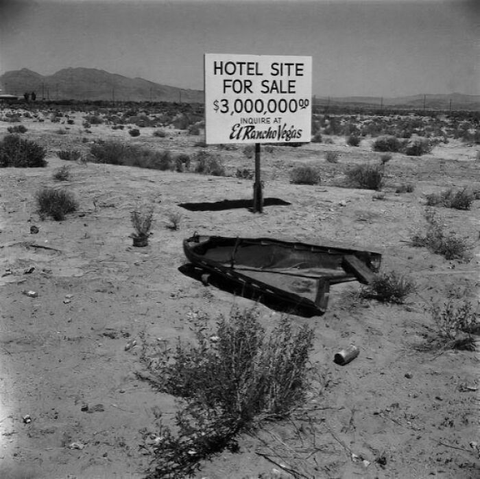 Desert landscape with a hotel site for sale sign and a broken rowboat, capturing fascinating photos and stories.