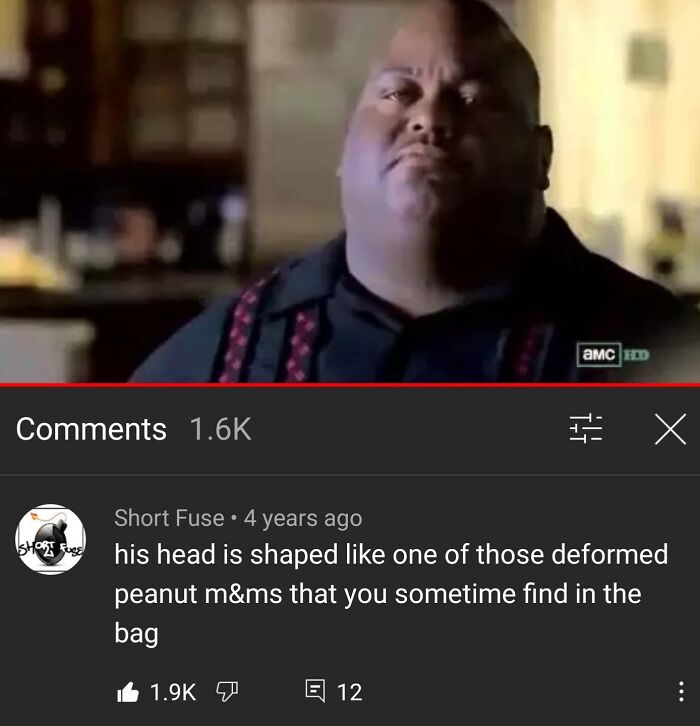 Man smirking in a video with a hilarious YouTube comment about his head shape shown below the frame.