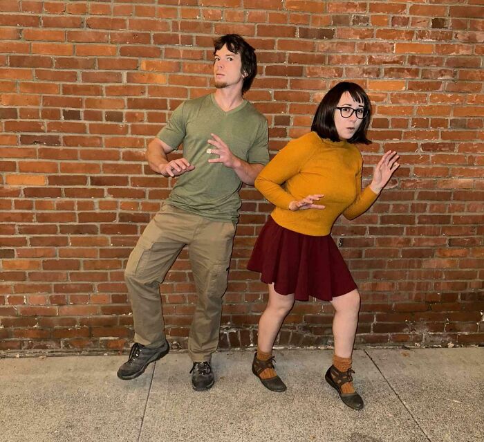 Two people dressed in genius Halloween costumes inspired by cartoon characters, posing against a brick wall.