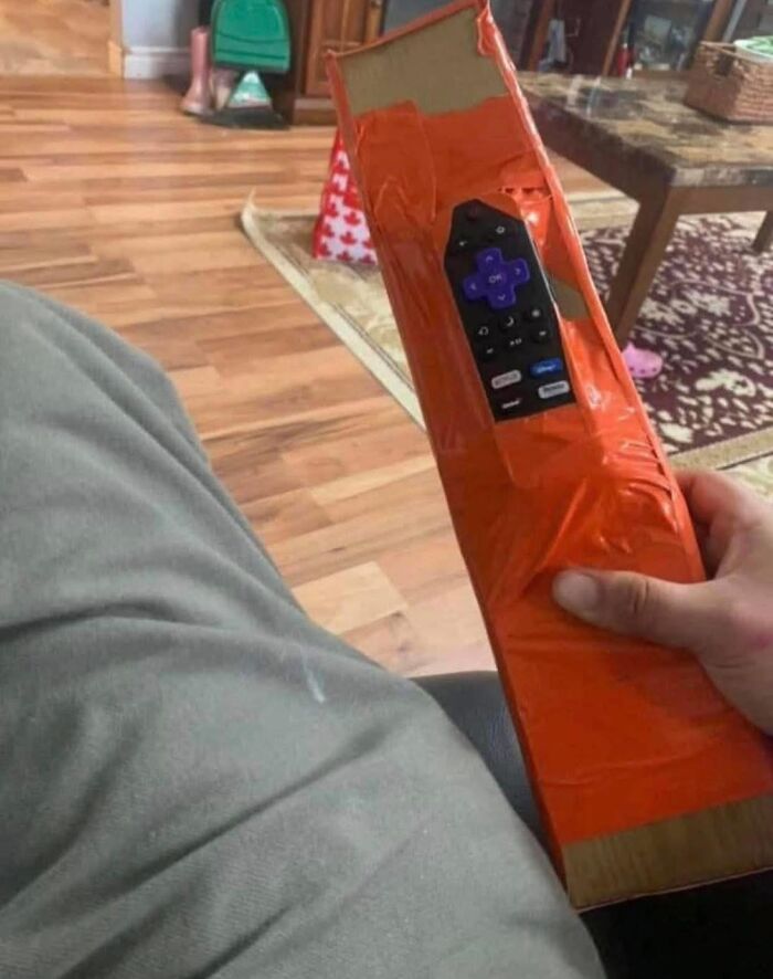 Hand holding a homemade remote control holder wrapped in orange tape, illustrating pleasures of the occult humor.