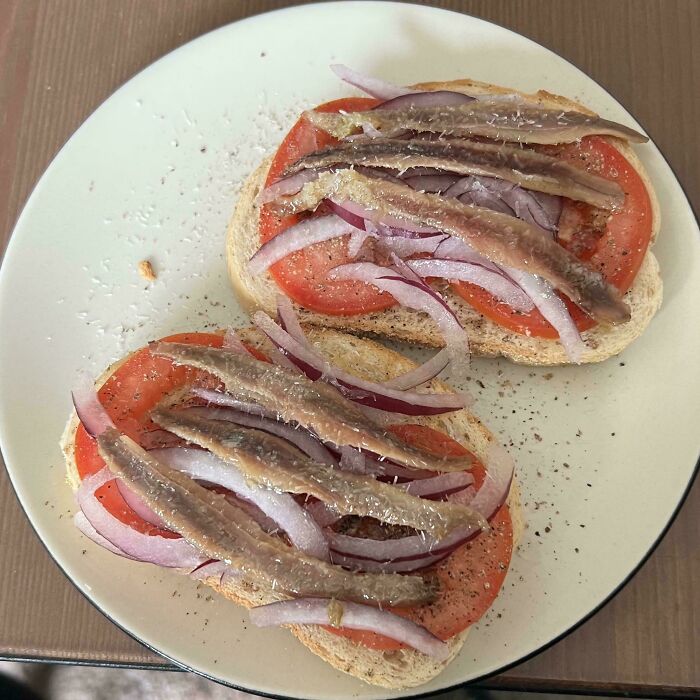 Open-faced sandwiches with tomato, red onion slices, and anchovies on white bread, a cursed and disgusting food picture.