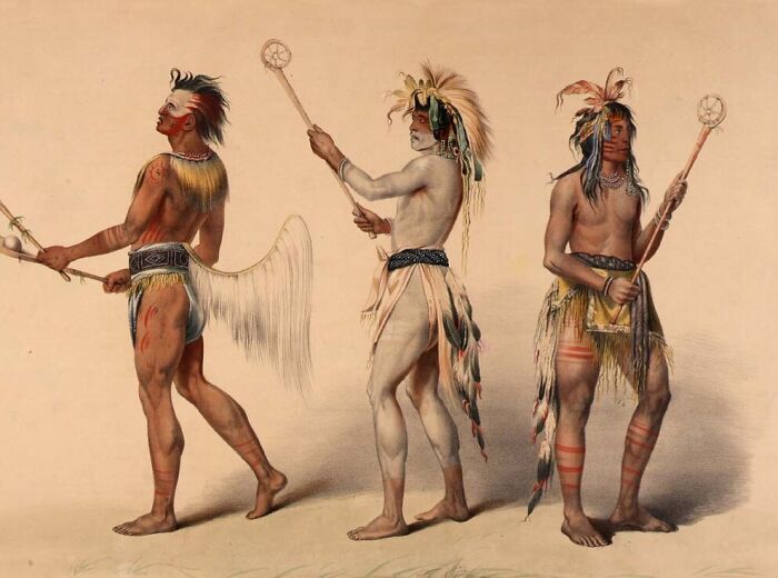 Three Indigenous men in traditional attire holding sticks, representing dangerous and unsafe historical sports activities.