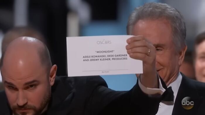 Man holding Oscar card showing wrong winner during award ceremony, a notable oopsie moment in hall of fame fails.