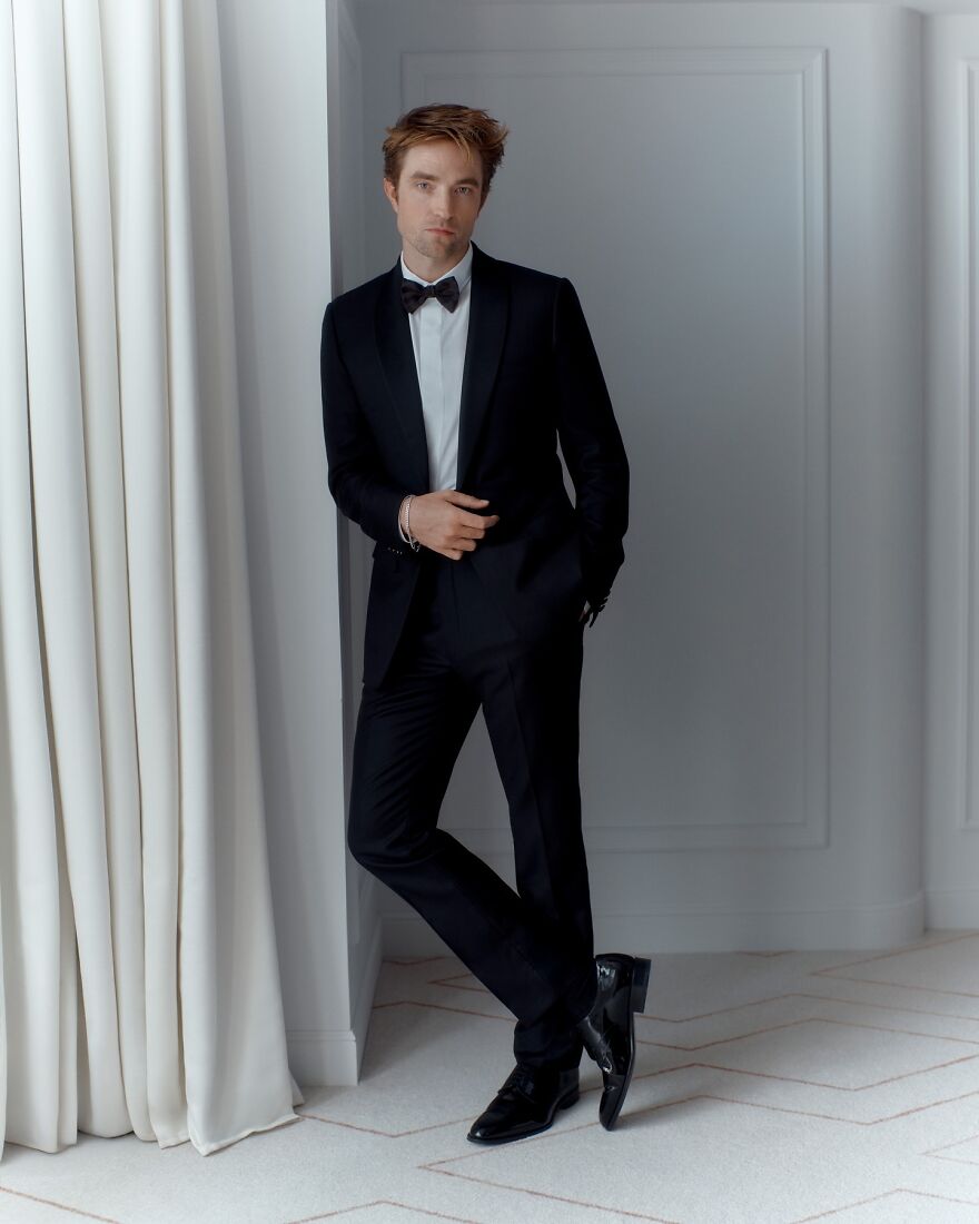 Robert Pattinson dressed in a black tuxedo posing indoors near white curtains for most handsome man in the world 2025.