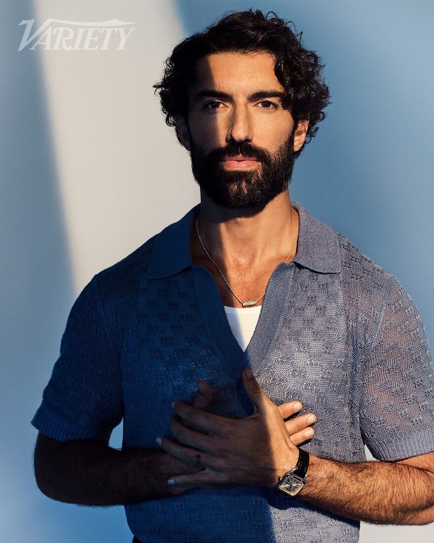 Justin Baldoni in textured blue shirt posing with hands crossed, representing most handsome man in the world 2025.