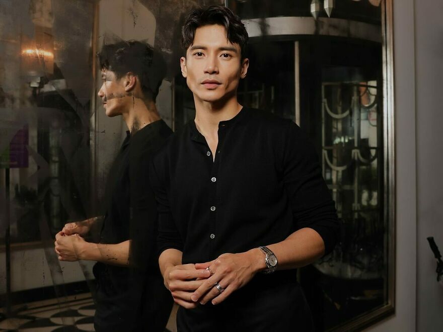 Manny Jacinto in black shirt posing by a reflective glass wall, representing the most handsome man in the world 2025 contest.