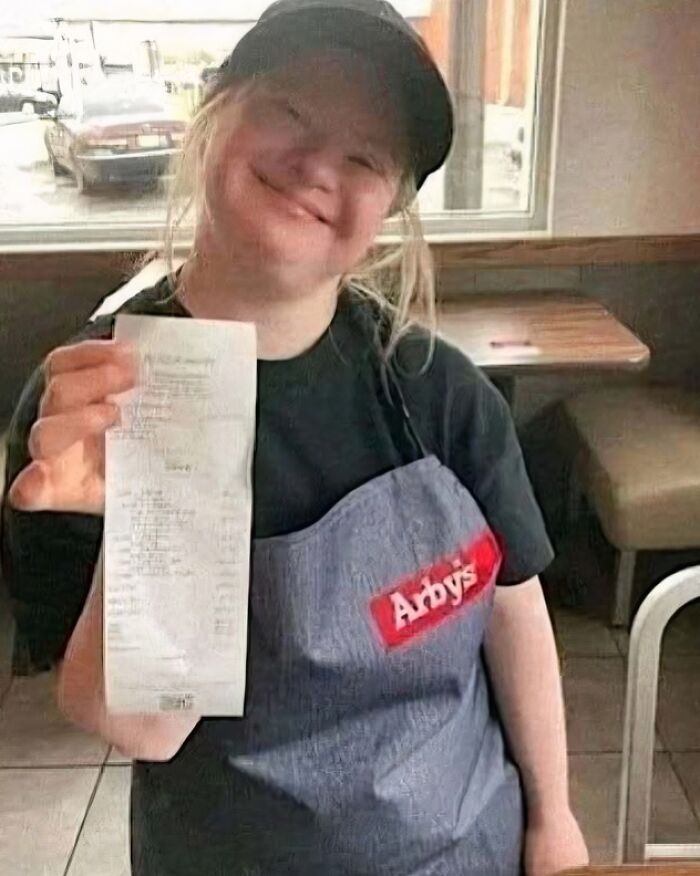 Smiling Arby’s employee holds receipt proudly, showcasing daily serotonin boost from positive work achievements.