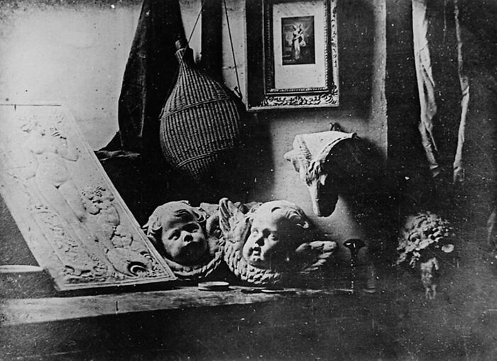 Early photography showing sculpted cherub heads and framed artwork in a dimly lit vintage room.