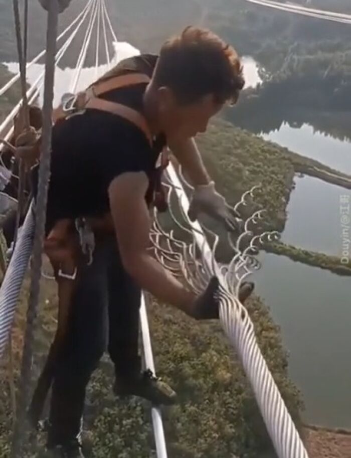 Worker in a safety harness repairing high-voltage cables precariously above a tall structure in unsettling job conditions.