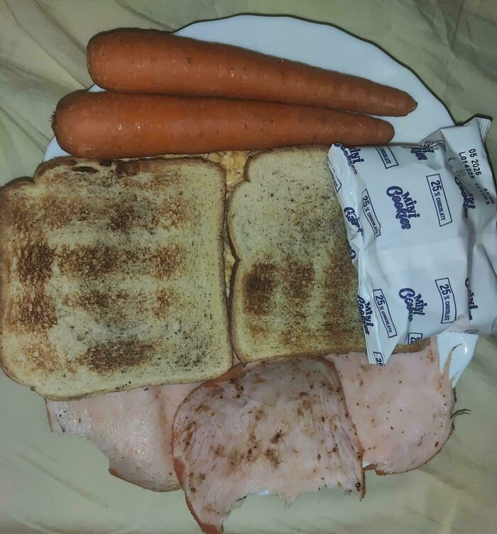 Plate with toasted bread, sliced deli meat, two carrots, and packaged mini cookies showing cursed and disgusting food.