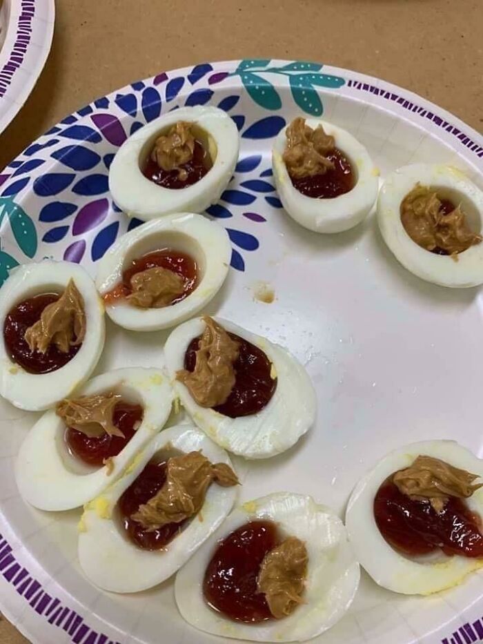 Sliced boiled eggs topped with peanut butter and jelly on a paper plate, a cursed and disgusting food combination.