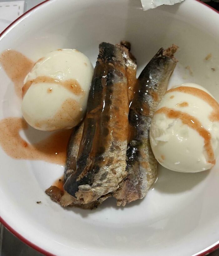 Boiled eggs with oily fish in a bowl, covered in a reddish-brown sauce, showing cursed and disgusting food presentation.