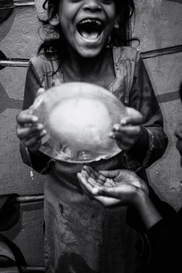 Black-and-white photo of a joyful child holding a bowl on the streets of India, capturing candid street life moments.