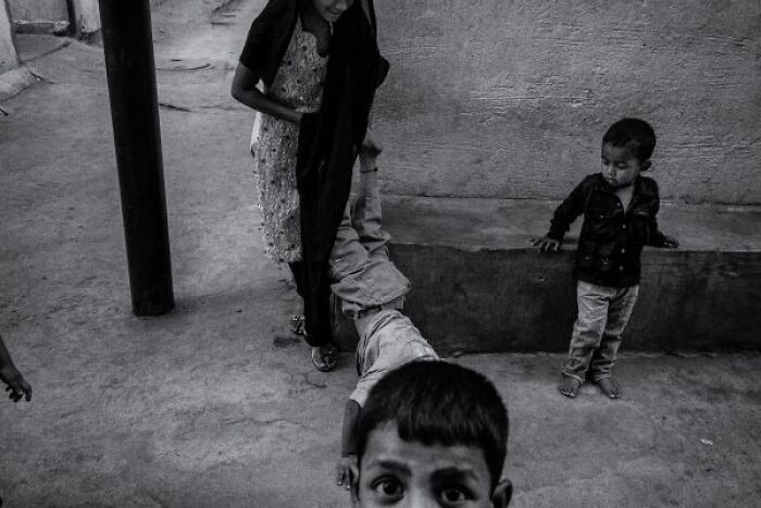 Black-and-white street photo from India showing children playing in a narrow alley with textured walls and pillars.