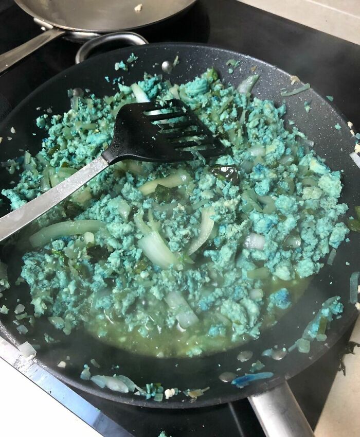 Blue scrambled eggs with onions in a frying pan, showing a cursed and disgusting food appearance.
