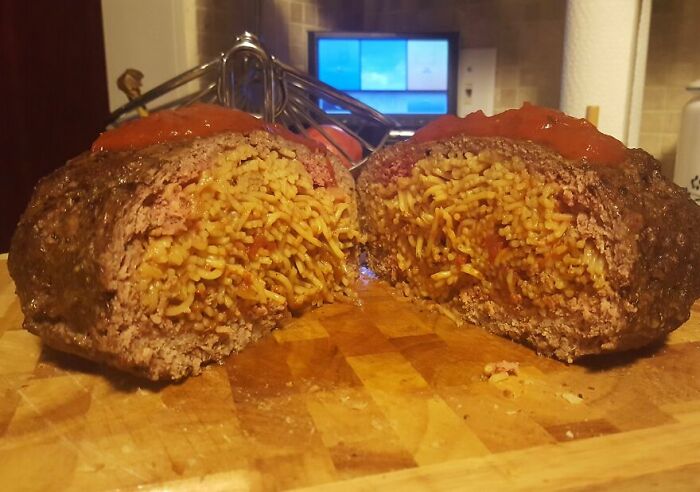 Close-up of a cursed and disgusting food picture showing a meatloaf stuffed with cooked noodles and topped with sauce.