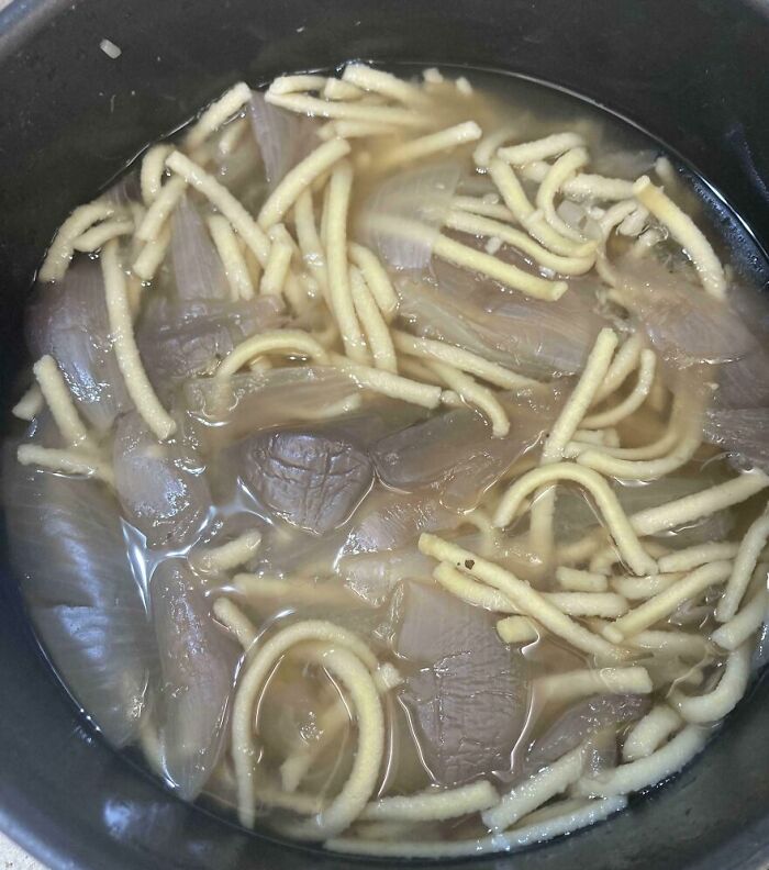 Disgusting food dish with pale slimy noodles and translucent, gelatinous chunks in murky liquid, evoking a cursed food image.
