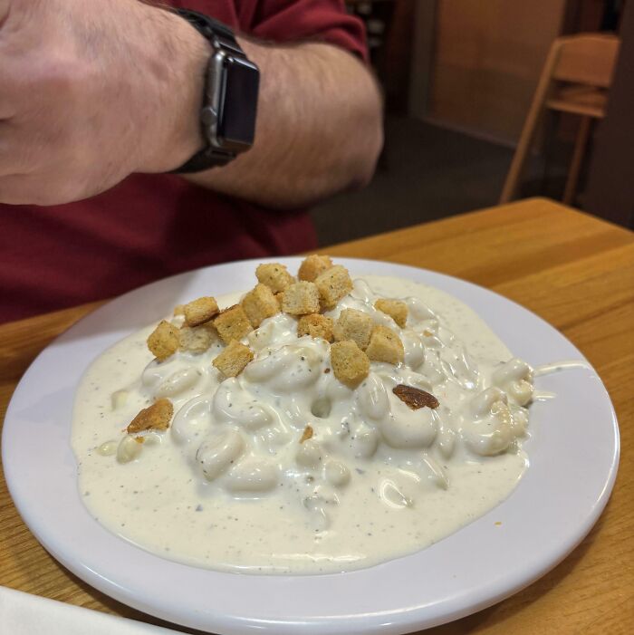 Plate of macaroni and cheese covered in excessive white sauce and topped with croutons, a cursed and disgusting food image.