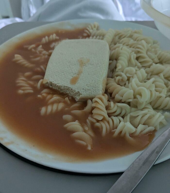 Plate of soggy rotini pasta in watery sauce with an unappetizing, partially eaten biscuit on top, cursed food image.