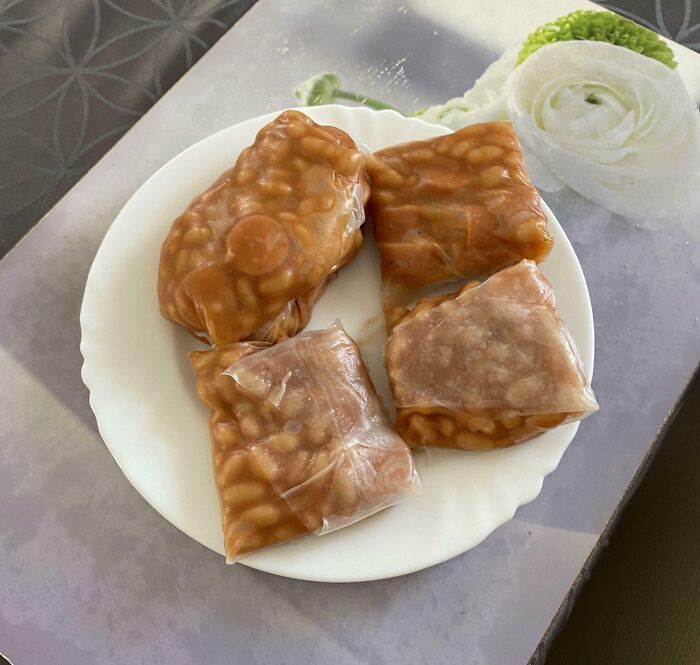 Four portions of canned beans in plastic wrap on a white plate, representing cursed and disgusting pictures of food.