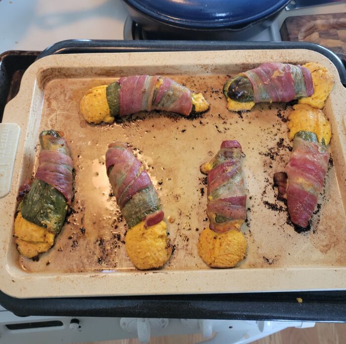 Baked stuffed jalapeños wrapped in bacon on a baking tray, an example of cursed and disgusting food.