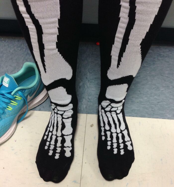 Person wearing black socks with skeleton foot bones design next to a blue sneaker, illustrating Halloween fails.