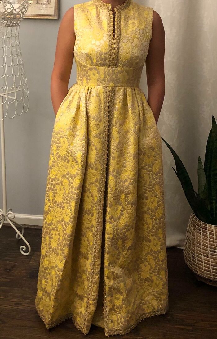 Sleeveless vintage yellow floral brocade dress with intricate trim, worn by a person standing indoors near a plant basket.