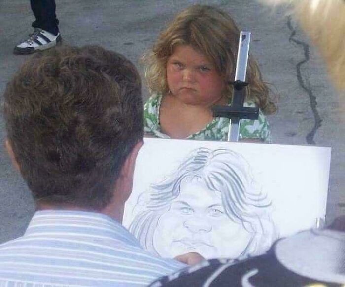Young girl with a serious expression sitting outdoors while a man draws a humorous caricature sketch of her face.