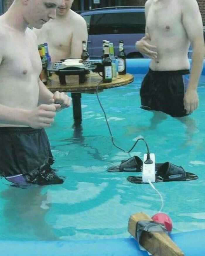 Three shirtless young men standing in a pool near a floating grill powered by an extension cord and shoes, funny people go hard.